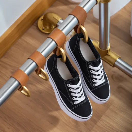 Anwendungsbeispiel Garderobe im Industrie-Look: Relinghaken mit Lederschlaufe in Camel an einer Rohrstange, daran schwarze Sneaker. Symbolfoto f�r den Lavane Relinghaken in Messing matt Design f�r Rohr � 19 und 25,4 mm.